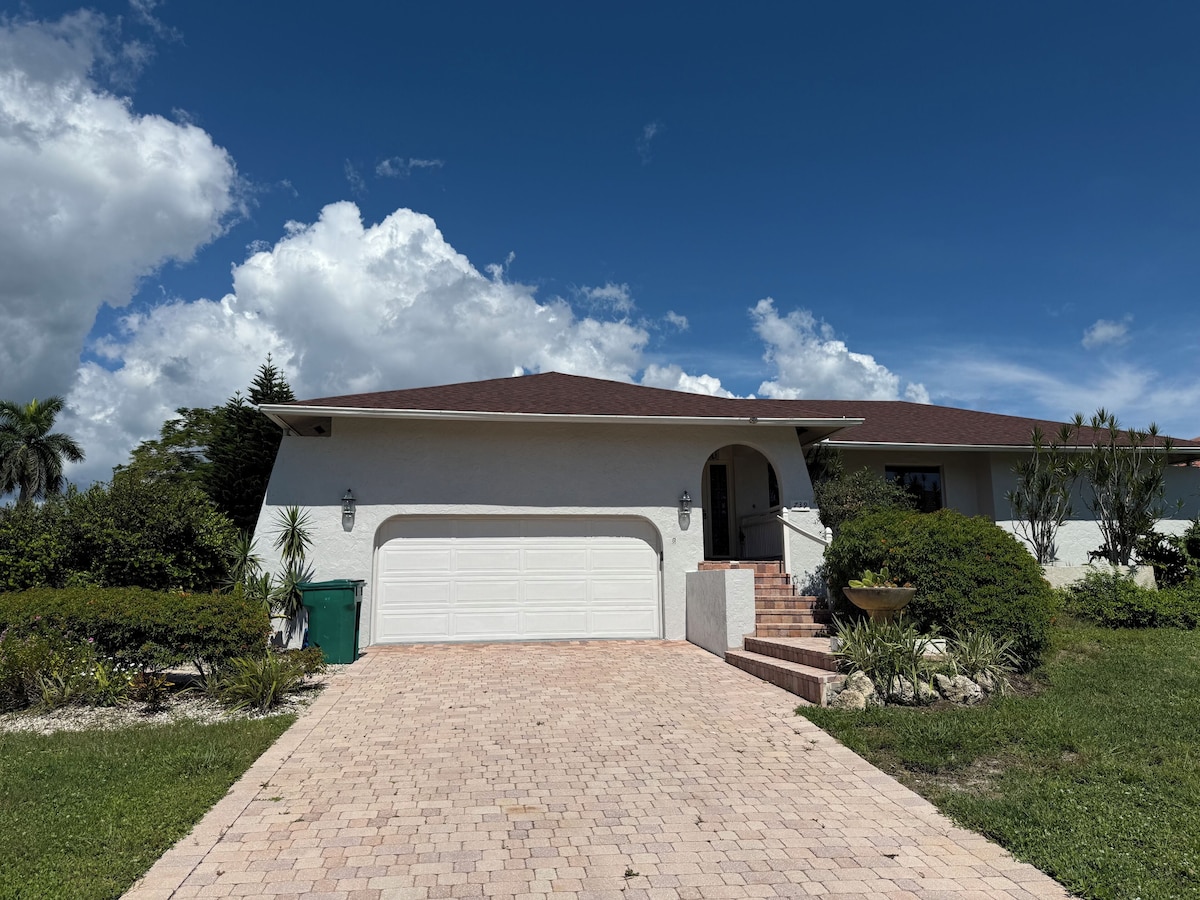 A single-story house with a white exterior, a red-tiled roof, and a brick driveway leading to a white garage.