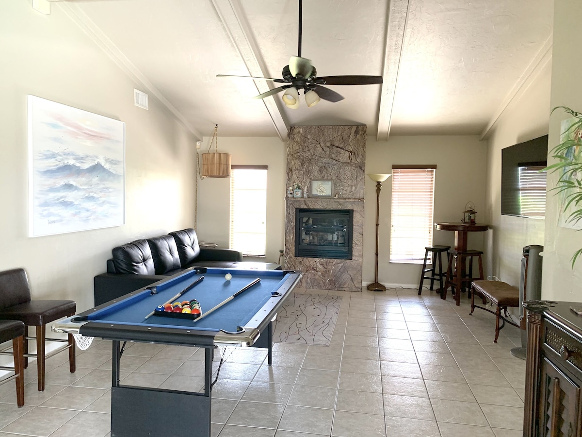 A room with a pool table, a leather sofa, a fireplace, and a ceiling fan.