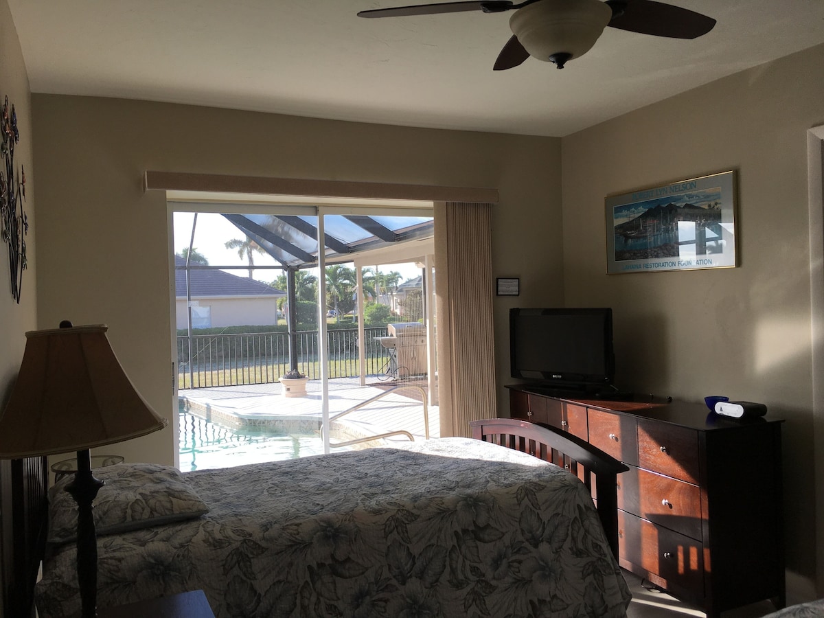 A hotel room with a bed, a TV, a dresser, and a view of the outside.