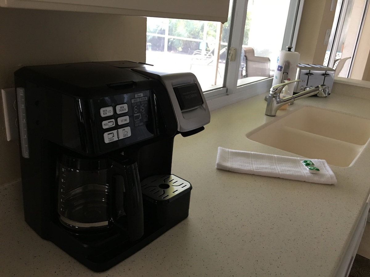 A coffee maker on a kitchen counter with a window in the background.