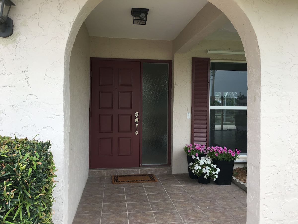 A front entrance with a red door, a glass door, and a potted plant with pink flowers.