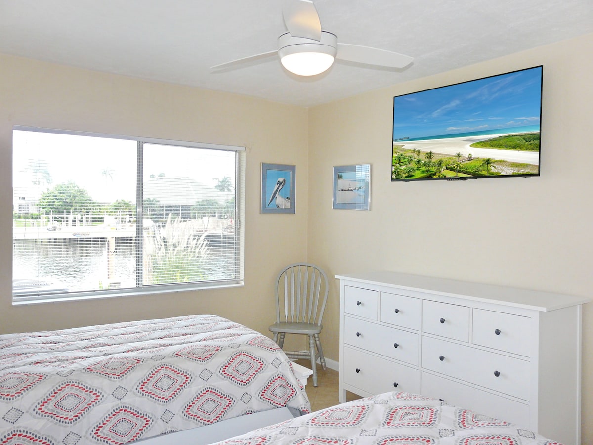 A bedroom with a bed, a dresser, a chair, and a large window with blinds.