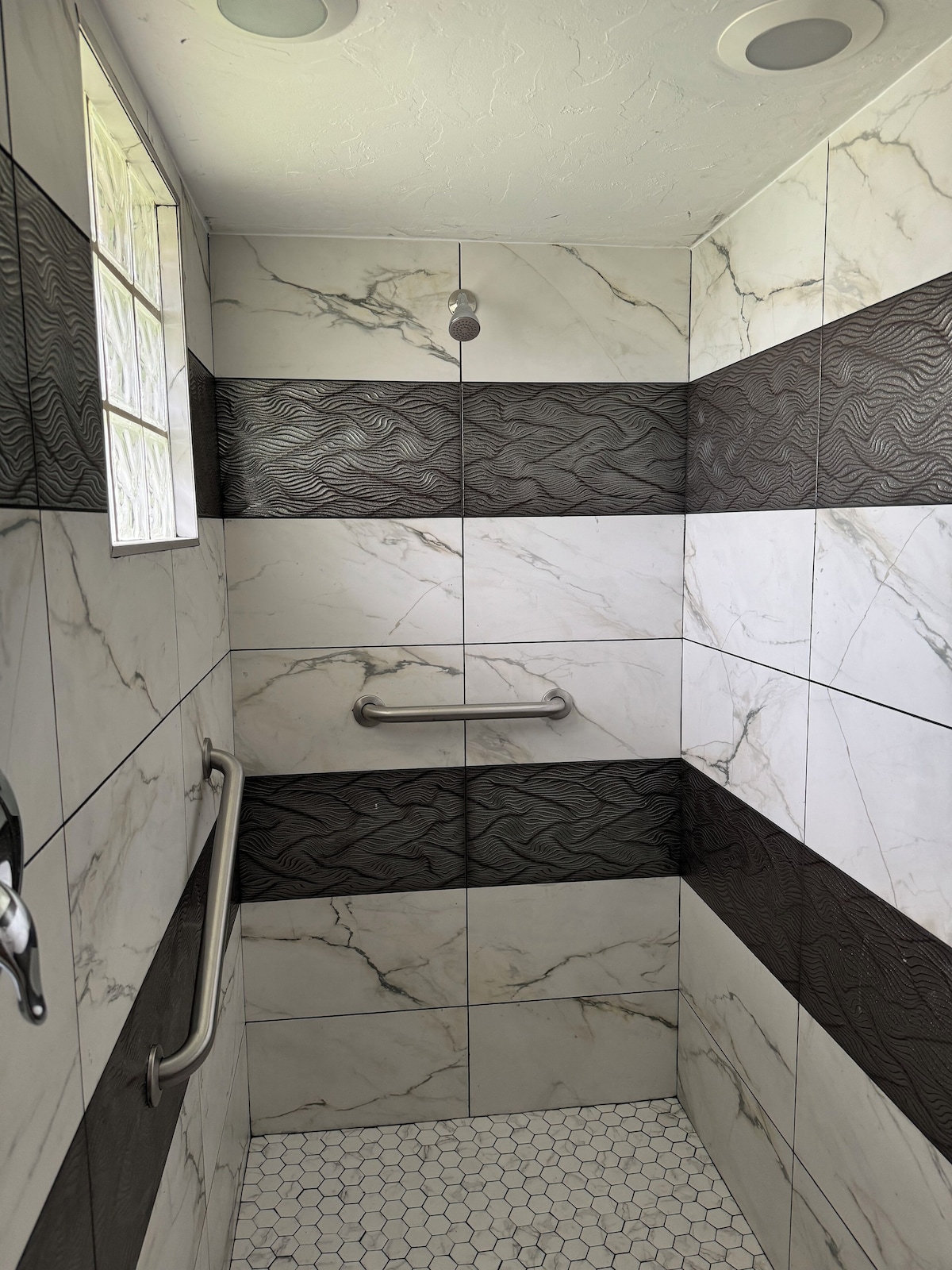 A shower with a handrail, patterned tiles, and a hexagonal tile floor.