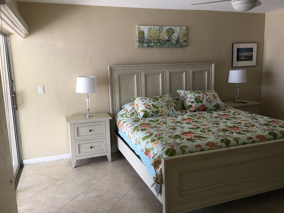 A bedroom with a bed, nightstands, lamps, and artwork on the walls.