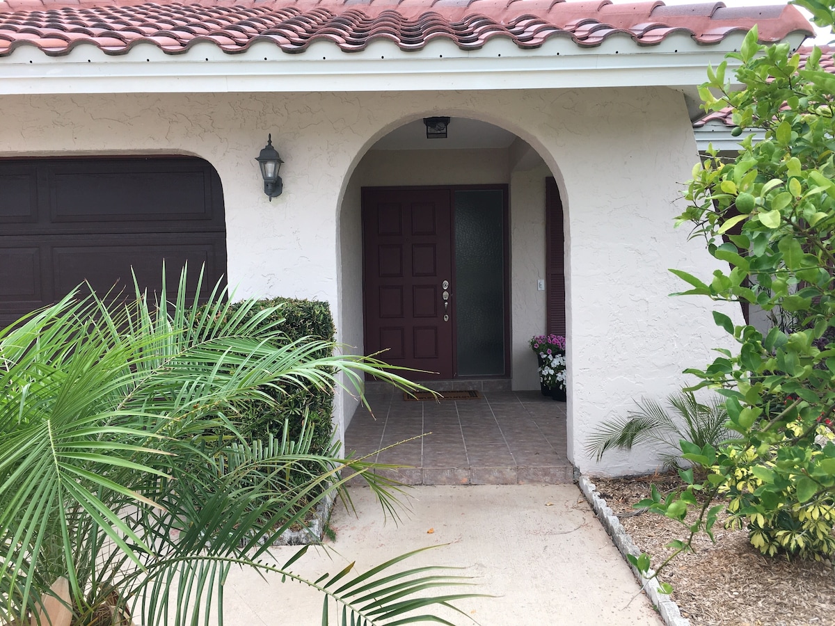 A house with a red-tiled roof, a dark brown door, and a small porch with a potted plant.