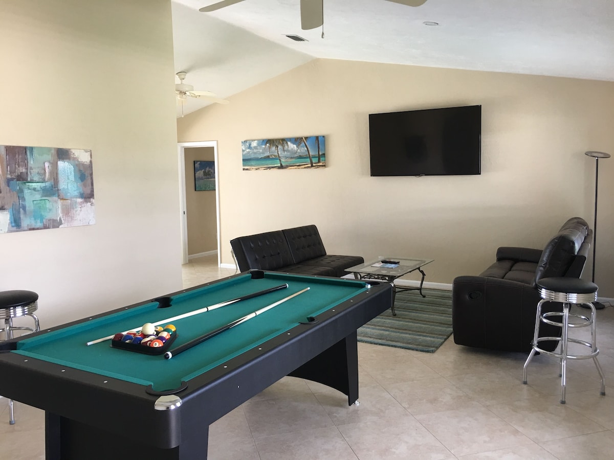 A pool table with balls, a sofa, a television, and artwork on the walls.