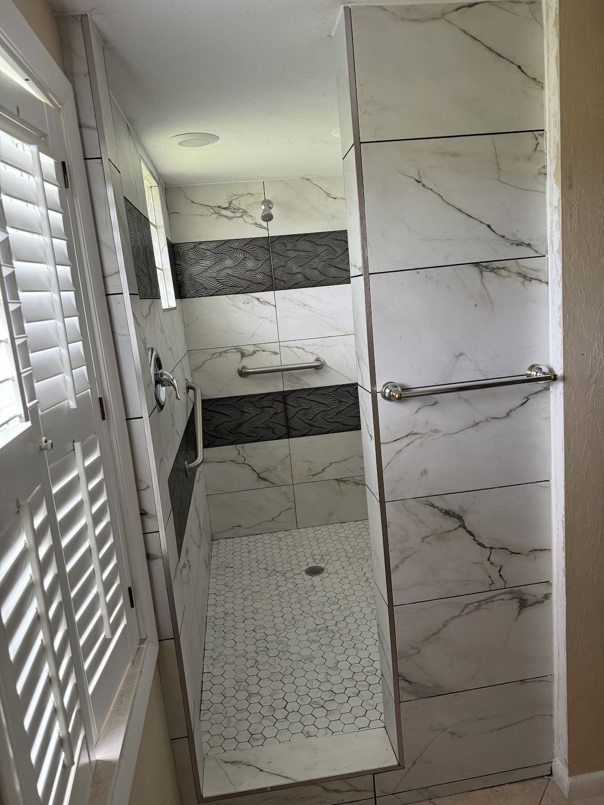 A narrow shower area with a glass door, a handrail, and a ceiling with a light fixture.