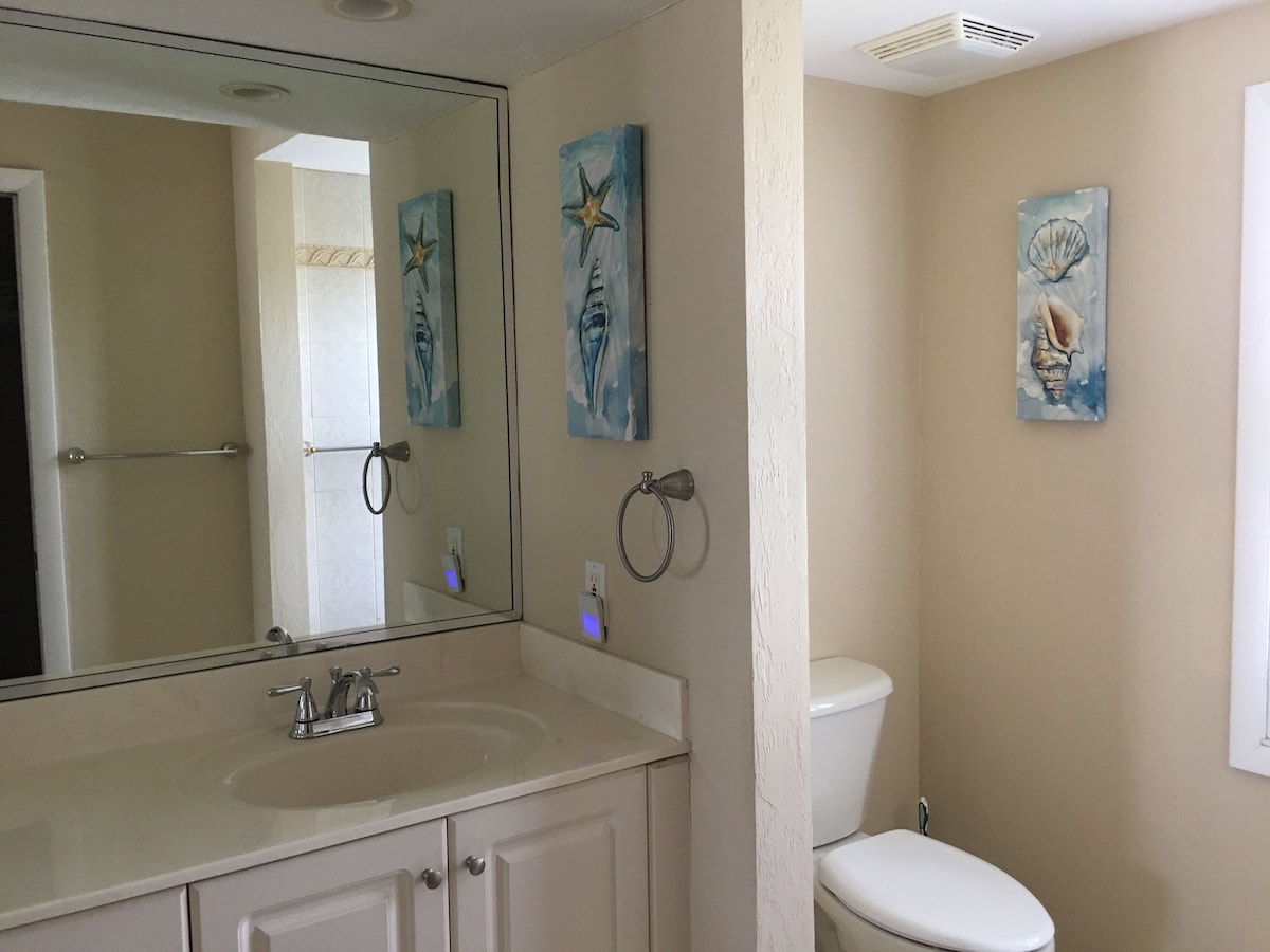 A bathroom with a sink, mirror, toilet, and wall-mounted artwork.