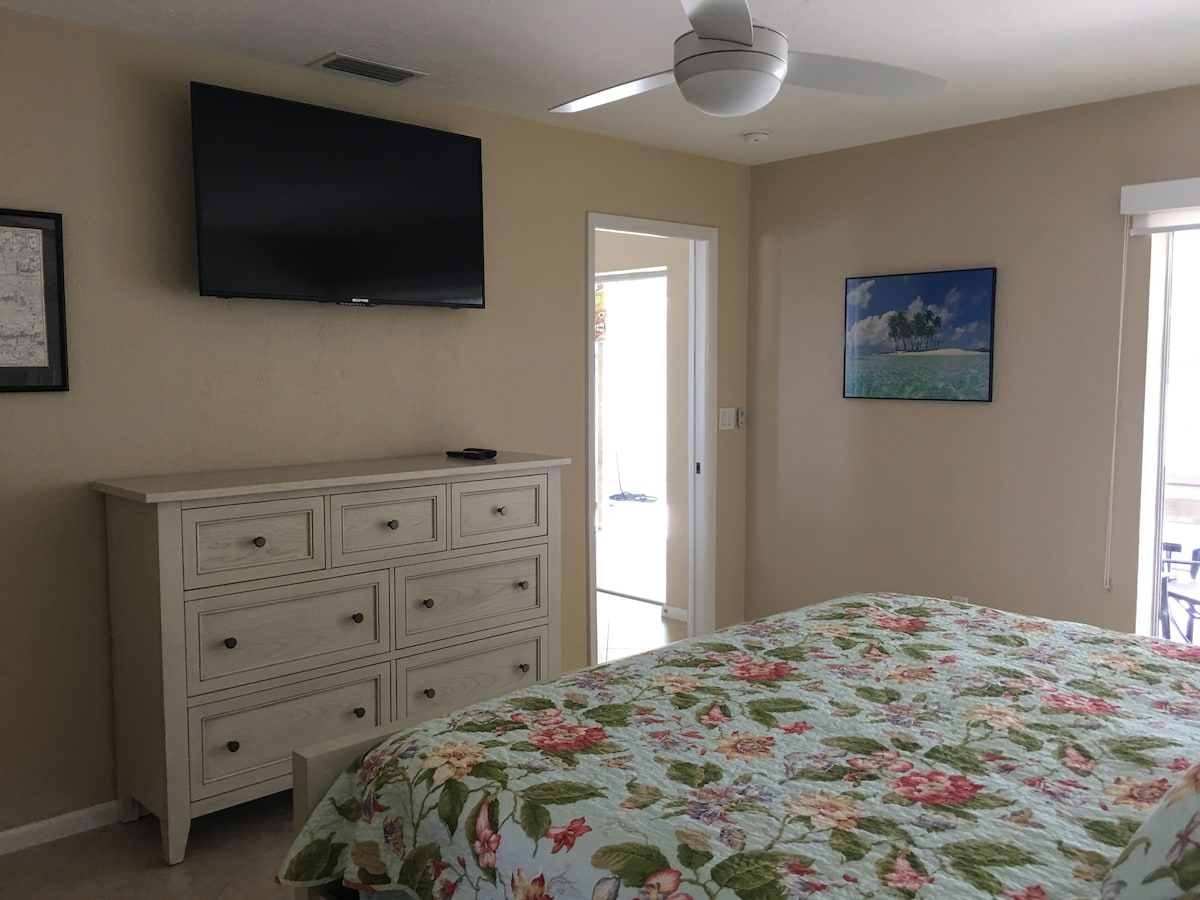 A bedroom with a bed, a dresser, a television, and a painting.